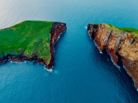 Aerial view of verdant green meets jagged cliffs, where the island splits into two distinct landmasses amidst the deep blue sea, Ilheus das Cabras, Terceira, Azores, Portugal.