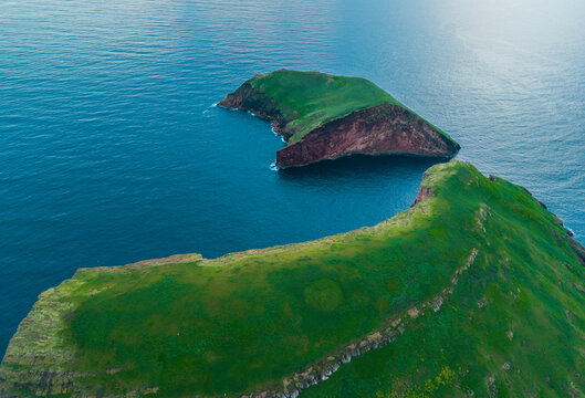 Aerial view of the stark contrast between the lush green of the island and the deep blue of the surrounding Atlantic, Ilheus das Cabras, Terceira, Azores, Portugal.