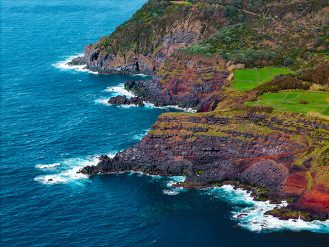 Aerial view of the dramatic cliffs where verdant slopes meet the turbulent azure sea, a stunning contrast of colors and textures, Ilheus das Cabras, Terceira, Azores, Portugal.