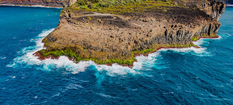 Aerial view of the rugged coastline of Ilheus das Cabras island where the dark volcanic rock meets the turquoise sea, Terceira, Azores, Portugal.