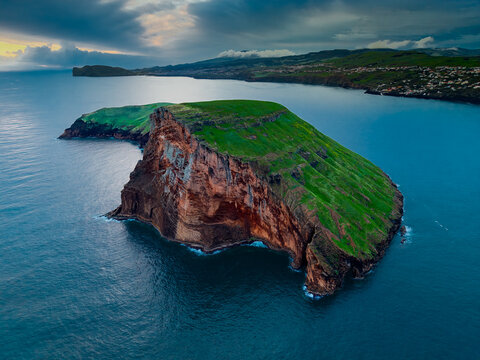 Aerial view of the dramatic cliffs of Ilheus das Cabras islet, a vibrant green crown against the deep blue sea, Terceira, Azores, Portugal.