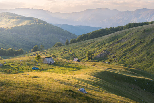View of sun-kissed meadows and distant peaks create a serene landscape with small huts nestled in the rolling hills, Foca, Bosnia and Herzegovina.