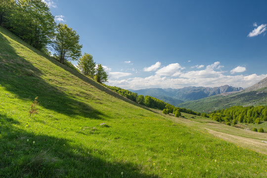 View of the vibrant green hillside meeting the distant mountains under a blue sky with scattered clouds, Foca, Republika Srpska, Bosnia and Herzegovina.