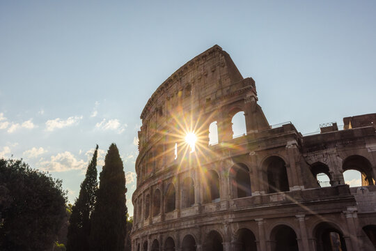 Sunburst through Colosseum arches in Rome with historic facade and clear blue sky
