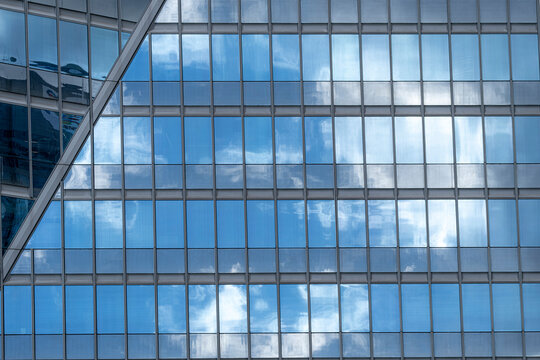 Modern corporate windows facade of glass reflection in grid pattern with clouds and sky creating a clean architectural business background