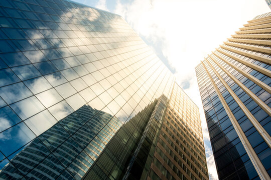 Upward view of modern corporate skyscraper facade with glass reflection in urban architecture catching sunlight for business background