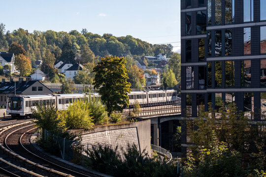Metro follows a curve along Brynseng tracks with suburb cityscape in Oslo Norway as rail transport sweeps through sunlit greenery today