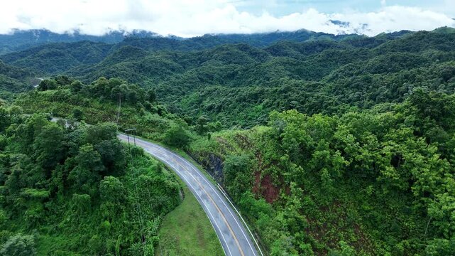 Aerial view highway Drone flying above winding road during sunlight, Winding asphalt road through tropical rainforest. countryside landscape. Landmark tourist attractions in Nan Province, Thailand.	