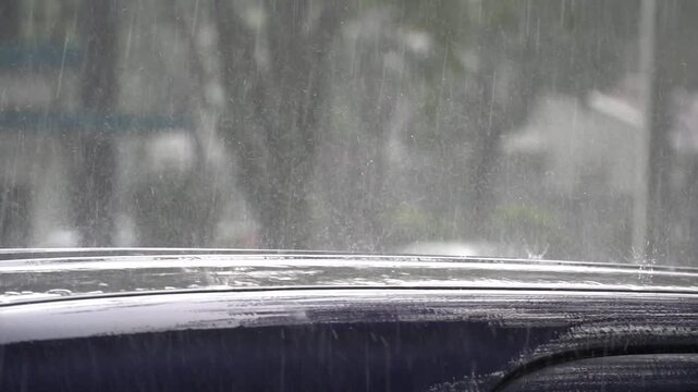 Rain falls heavily on a car's windshield and roof during a stormy day in the city.