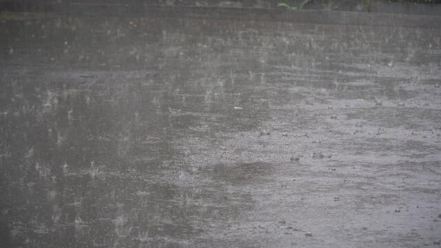 Rain falls heavily on a wet city street causing flooded roads