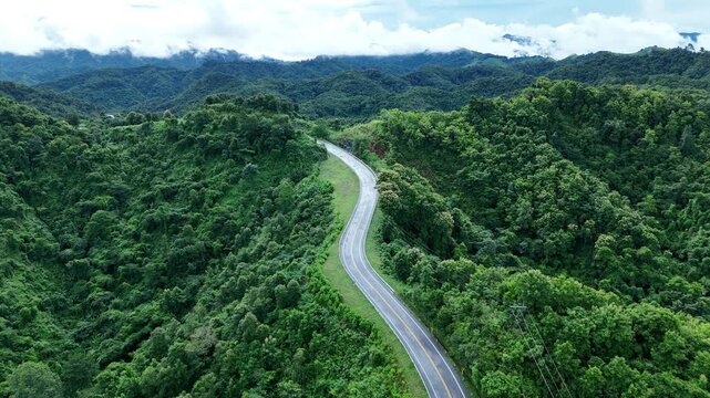 Aerial view highway Drone flying above winding road during sunlight, Winding asphalt road through tropical rainforest. countryside landscape. Landmark tourist attractions in Nan Province, Thailand.	