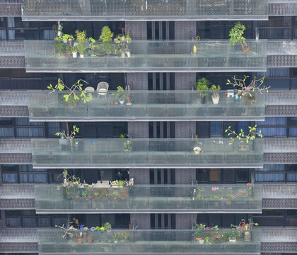 Aerial view of modern apartment building balconies decorated with lush potted plants and small trees on a dark textured facade in Taiwan.