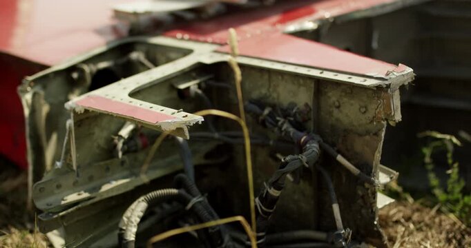 Close up view of damaged aircraft structural components with exposed hydraulic lines and wires in a salvage yard