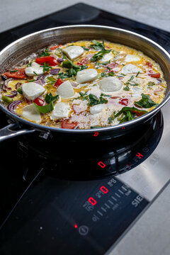Cooking an italian frittata with mozarella, asparagus, eggs, onions, tomatoes and fresh herbs in spring time at home in the kitchen