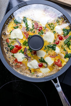 Cooking an italian frittata with mozarella, asparagus, eggs, onions, tomatoes and fresh herbs in spring time at home in the kitchen
