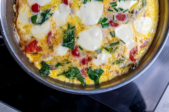 Cooking an italian frittata with mozarella, asparagus, eggs, onions, tomatoes and fresh herbs in spring time at home in the kitchen