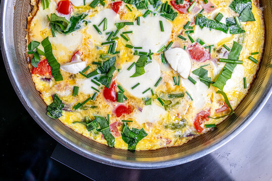 Cooking an italian frittata with mozarella, asparagus, eggs, onions, tomatoes and fresh herbs in spring time at home in the kitchen