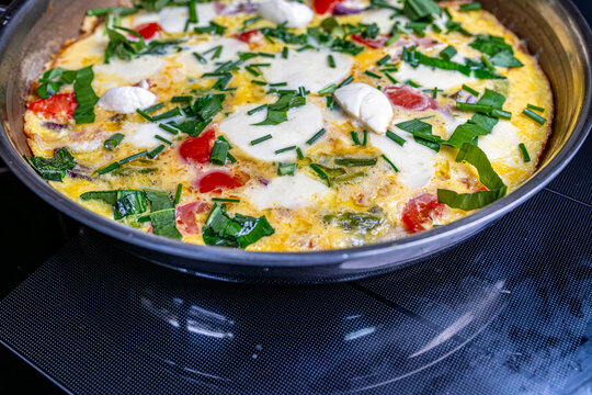Cooking an italian frittata with mozarella, asparagus, eggs, onions, tomatoes and fresh herbs in spring time at home in the kitchen