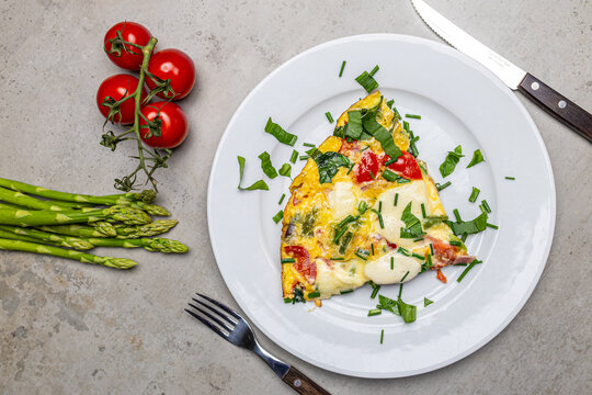 Cooking an italian frittata with mozarella, asparagus, eggs, onions, tomatoes and fresh herbs in spring time at home in the kitchen