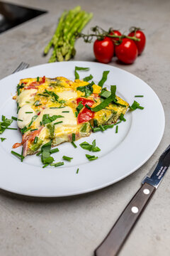 Cooking an italian frittata with mozarella, asparagus, eggs, onions, tomatoes and fresh herbs in spring time at home in the kitchen