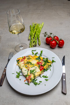Cooking an italian frittata with mozarella, asparagus, eggs, onions, tomatoes and fresh herbs in spring time at home in the kitchen