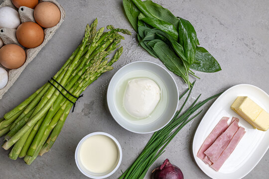 Cooking an italian frittata with mozarella, asparagus, eggs, onions, tomatoes and fresh herbs in spring time at home in the kitchen