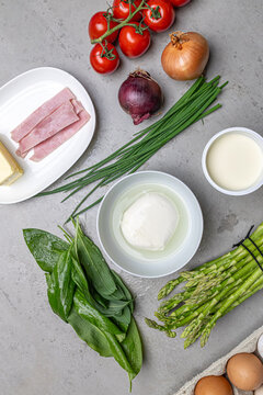 Cooking an italian frittata with mozarella, asparagus, eggs, onions, tomatoes and fresh herbs in spring time at home in the kitchen