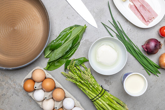 Cooking an italian frittata with mozarella, asparagus, eggs, onions, tomatoes and fresh herbs in spring time at home in the kitchen