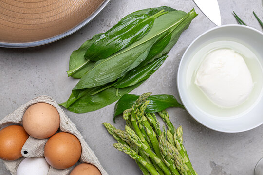 Cooking an italian frittata with mozarella, asparagus, eggs, onions, tomatoes and fresh herbs in spring time at home in the kitchen