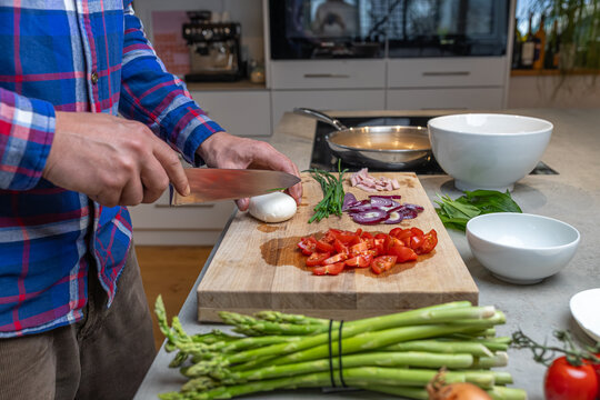 Cooking an italian frittata with mozarella, asparagus, eggs, onions, tomatoes and fresh herbs in spring time at home in the kitchen