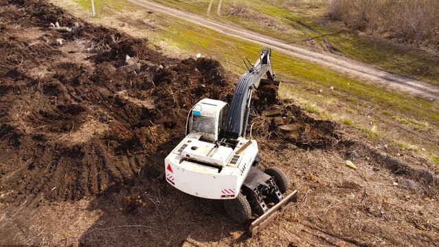 drone photograph of a white wheeled excavator in the process of clearing and leveling earth.