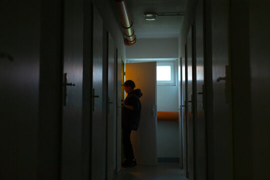 worker in warm lit hallway using device, courier pauses in amber glow near doorway to scan or confirm order, red and yellow tones accent narrow corridor with industrial pipes, pragmatic