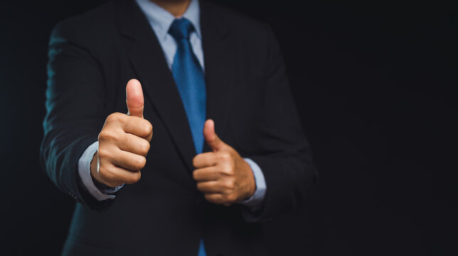 Businessman showing thumbs up gesture on dark background