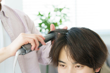 Naklejka premium ヘアアイロンで髪をカールする若い日本人美容師の手元のアッ