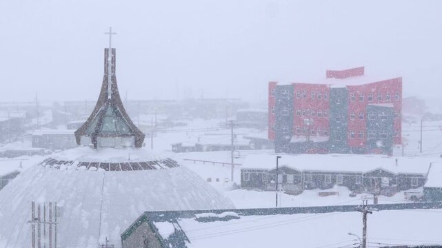 St. Jude's Cathedral with residential housing and the Qajuqturvik food center in the background during heavy snow.