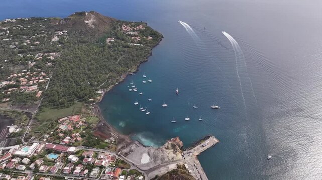 Drone flying left capturing Vulcano bay with anchored yachts, coastline and island village.