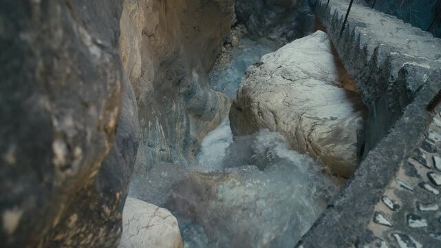 Clear water flowing through a narrow rocky canyon with visible stone textures and a concrete stairs. Natural and rugged environment combined with subtle human infrastructure detail.