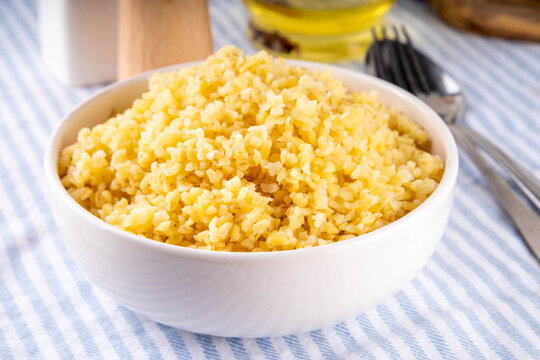 Boiled cooked bulgur pilaf, healthy wheat garnish, side dish, in white ceramic plate on the kitchen table