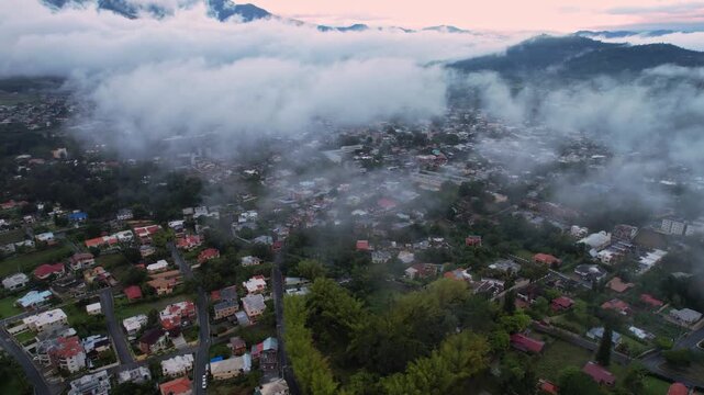 Amazing drone shot of Jarabacoa town residential neighborhood covered partially by low clouds and fog in early sunrise, La Vega, Dominican Republic