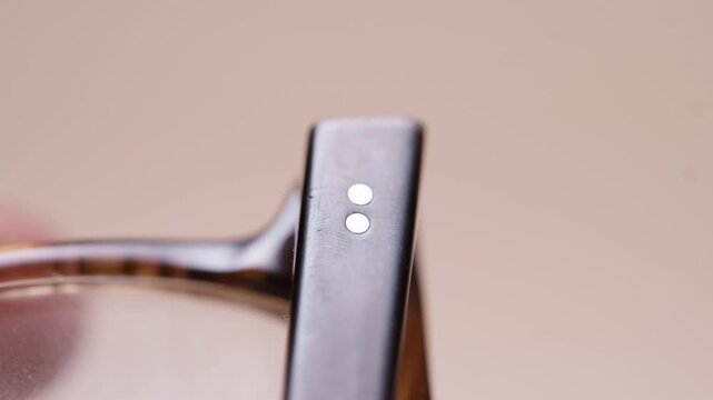 Extreme close-up of a hand holding old broken eyeglasses and closely inspecting the hinge. Damaged frame detail clearly visible. Authentic DIY repair assessment footage.