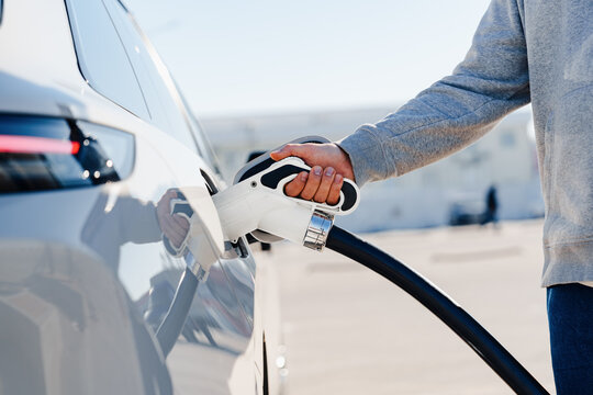 Person uses electric car charger at charging station during the day