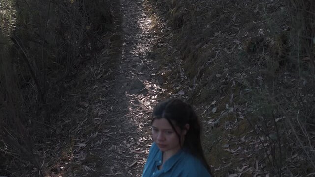 Captivating jib shot of a woman in a blue shirt standing on a rugged path at Warrandyte Mining Mountain, Melbourne. Natural lighting enhances the serene outdoor setting.