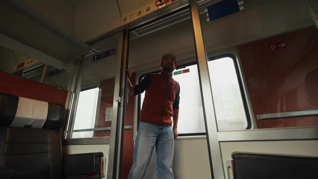 A Man Stands by the Sliding Doors Inside a Train Carriage, Looking Inward as Light Streams Through the Windows - Medium Shot