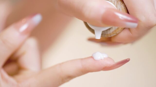 Close up woman hands finger squeezing dropping white cream or oil lotion from pump bottle for skincare, self care of young healthy female apply creamy on hand after shower for moisturizing on skin