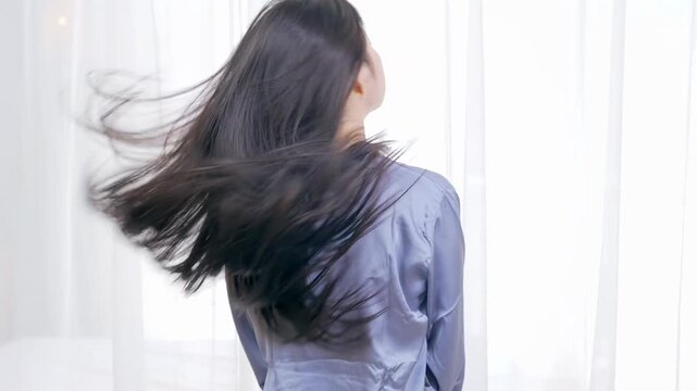 Back view of young woman swings head with flowing long moving hair movement showcasing trendy black fluttering gorgeous hair after visiting a beauty salon