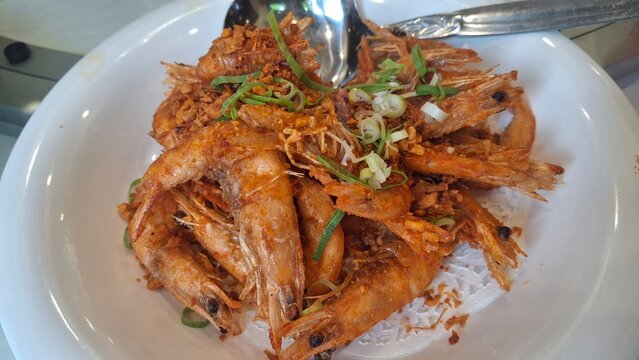 Close up of udang goreng bawang putih. Crispy fried shrimp tossed with aromatic garlic, delivering a golden texture and savory flavor. Rich, appetizing presentation with crunchy garlic bits and warm t