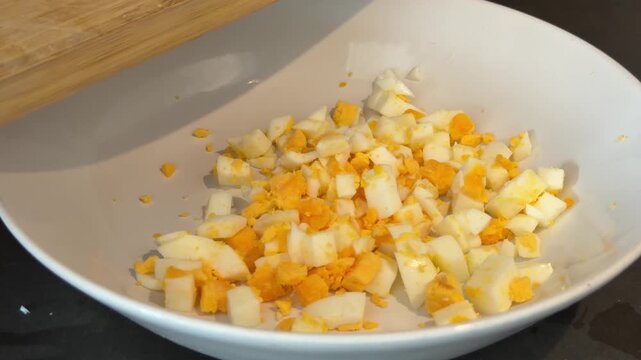 Diced hard boiled egg falling into a white bowl for a homemade recipe preparation, cooking healthy breakfast or salad with essential protein and nutritious ingredients