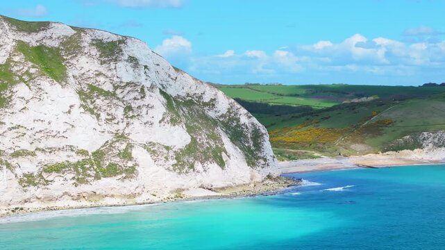 Tracking telephoto aerial shot of chalk cliffs and background farmland on Dorset's Jurassic coastline