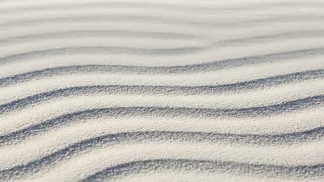 Repeating curved sand dunes of bright white sand with gentle shadows in the sunlight