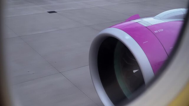 Commercial airplane engine with vibrant pink livery viewed from passenger window on airport runway. Jet turbine rotating during taxiing phase with aviation travel concept and airline industry